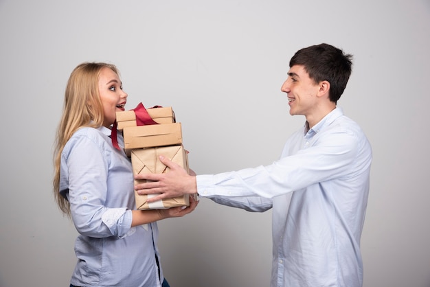 Glimlachende man verrast zijn vriendin met cadeautjes over grijze muur.