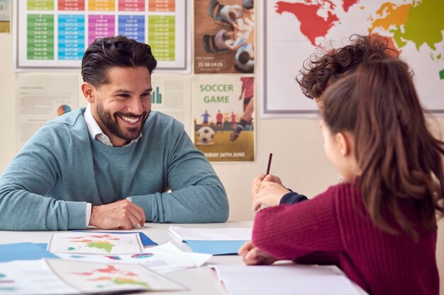 Glimlachende mannelijke basisschoolleraar die met studenten aan het bureau in de klas werkt