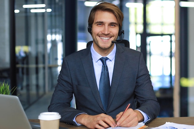 Glimlachende mannelijke business consultant met koptelefoon zittend op moderne kantoor video-oproep kijken naar laptop scherm Man klantenservice ondersteuning agent hulplijn praten online chat