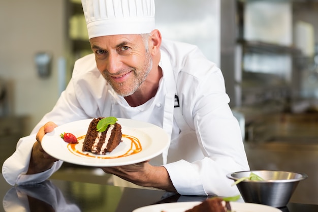 Glimlachende mannelijke gebakjechef-kok met dessert in keuken