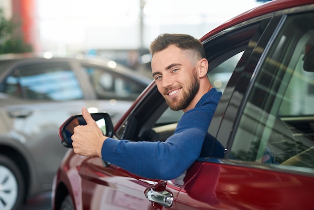 Glimlachende mens die duim in auto toont.