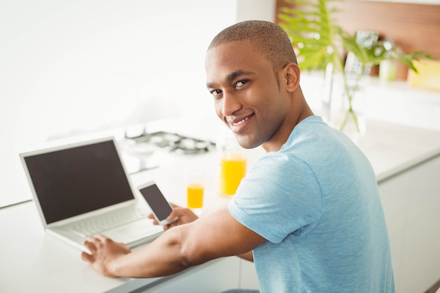 Glimlachende mens die laptop en smartphone in de woonkamer thuis met behulp van