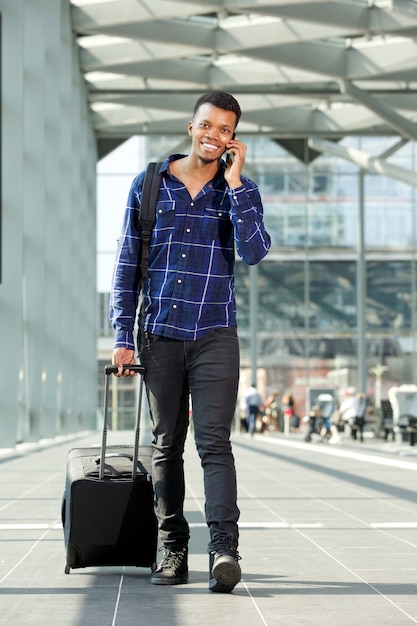 Glimlachende mens die met koffer loopt die op mobiele telefoon spreekt