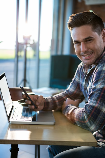 Glimlachende mens die mobiele telefoon met laptop op lijst met behulp van