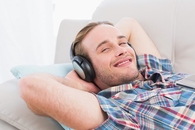 Glimlachende mens die op bank het luisteren muziek ligt