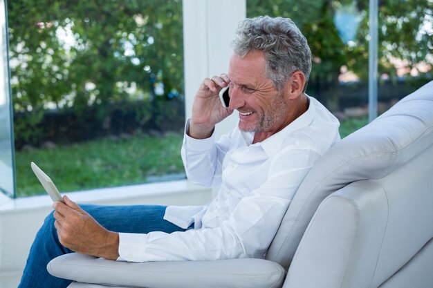 Glimlachende mens die op telefoon spreekt terwijl het houden van tablet