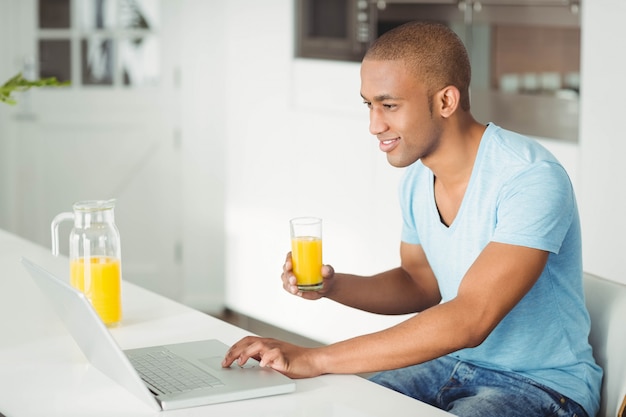 Glimlachende mens gebruikend laptop en drinkend jus d&#39;orange in ktichen