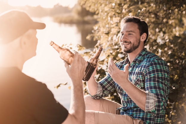 Glimlachende Mensen die Bier drinken dichtbij Rivier in de Zomer.