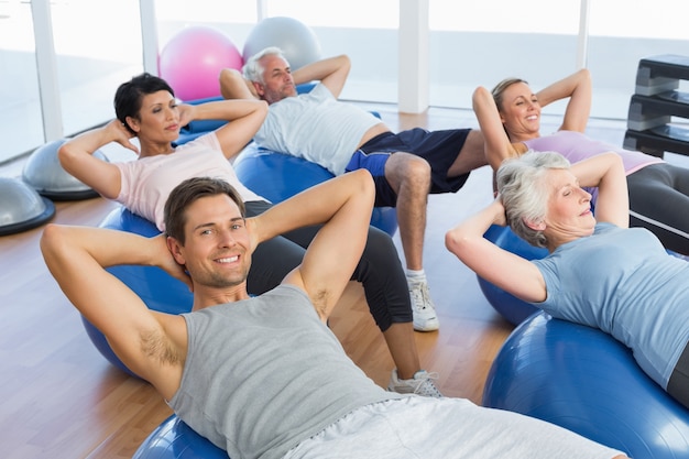 Glimlachende mensen die zich op oefeningsballen uitrekken in gymnastiek