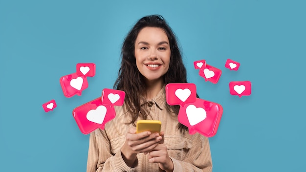 Glimlachende millennial europese vrouw heeft romantische chat met hartjes op smartphone geïsoleerd op blauwe studio achtergrond