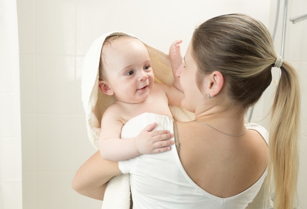 Glimlachende moeder die baby in handdoek bedekt na het baden