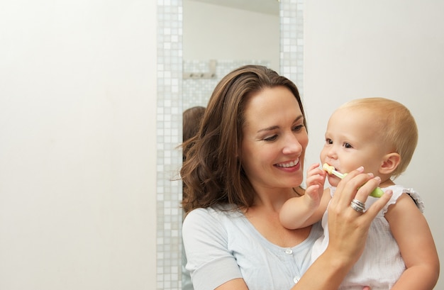 Glimlachende moeder die leuke baby onderwijzen hoe tanden met tandenborstel te borstelen