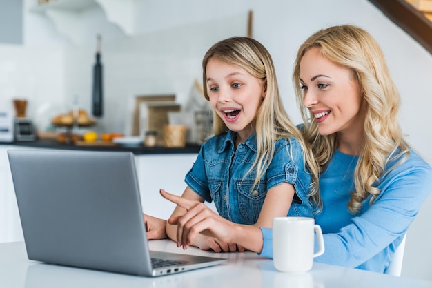 Glimlachende moeder met dochter die laptop in keuken met behulp van