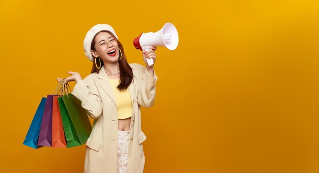 Foto glimlachende mooie aziatische tienervrouw met winkeltassen en aankondiging korting in megafoon