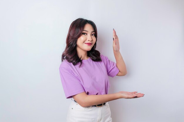 Glimlachende mooie Aziatische vrouw die met de vinger wijst naar lege ruimte naast haar geïsoleerde witte achtergrond
