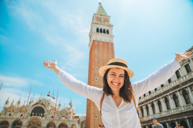 Glimlachende mooie blanke vrouw steekt handen op bij de klokkentoren Campanile di San Marco van Venetië op achtergrond