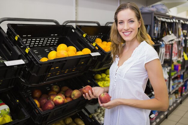 Glimlachende mooie blondevrouw die een appel kopen