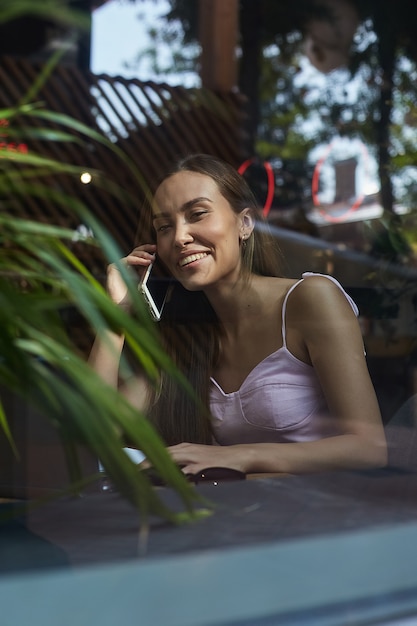 Glimlachende mooie dame die telefonisch belt, is door het raam buiten het café geschoten