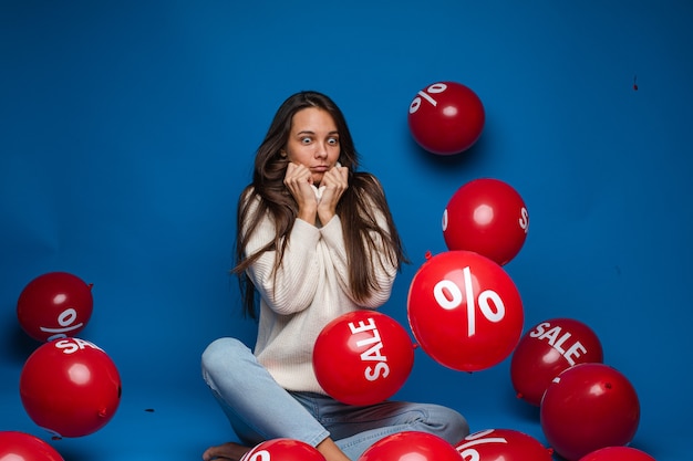 Glimlachende mooie dame met twee rode ballonnen, geïsoleerd op blauwe muur