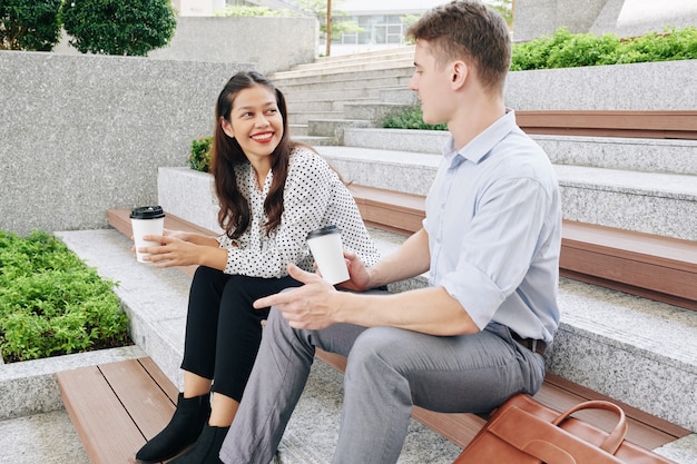 Glimlachende mooie jonge vrouw van gemengd ras kijken naar collega interessante verhaal vertellen wanneer ze buiten zitten