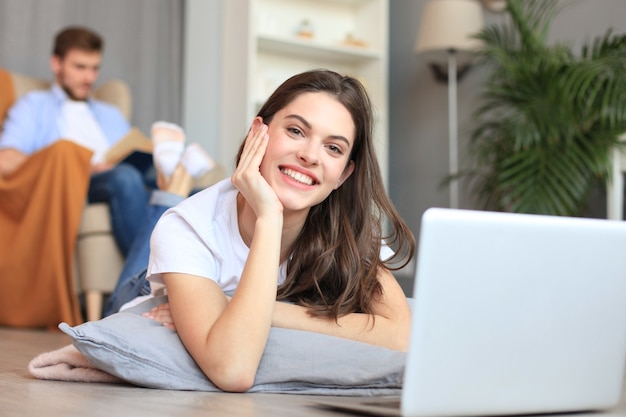 Glimlachende mooie vrouw die laptop met vage man op achtergrond thuis met behulp van.