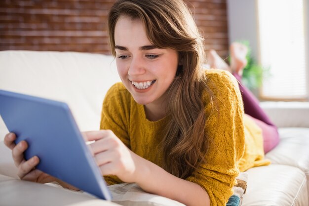 Glimlachende mooie vrouw die tablet op laag in de woonkamer met behulp van