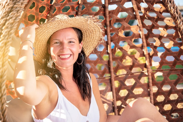 Glimlachende mooie vrouw met hoed die vrije tijd heeft bij strand