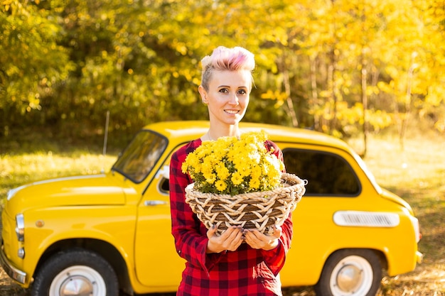 Glimlachende mooie vrouwenmand met bloemen en pompoenen op de achtergrond van het herfstpark dichtbij gele auto