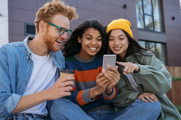 Glimlachende multiraciale vrienden met behulp van mobiele telefoon kijken naar video winkelen online