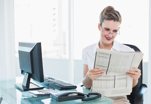 Glimlachende onderneemster die glazen draagt ​​die krant lezen