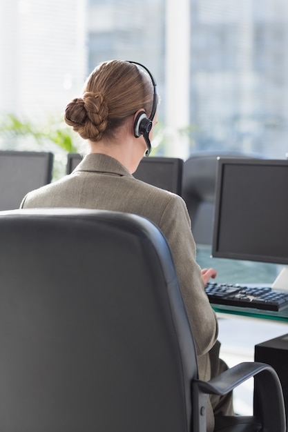 Glimlachende onderneemster met hoofdtelefoon die computers met behulp van