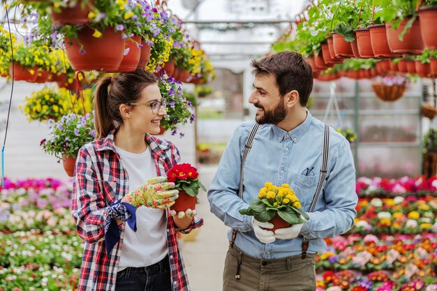 Glimlachende ondernemers staan in kas en houden potten met kleurrijke bloemen.