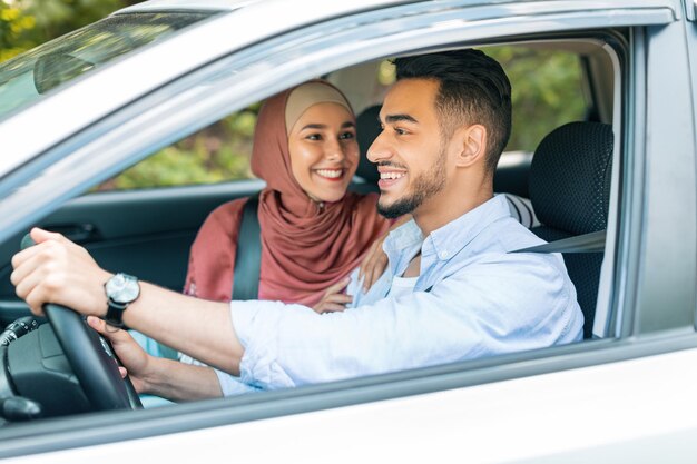 Glimlachende opgewonden duizendjarige midden-oosterse vrouw in hijab kijkt naar man aan stuur en heeft goed nieuws in auto