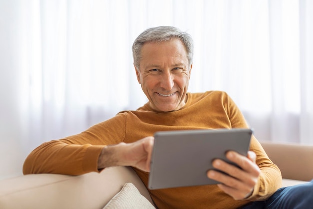Glimlachende oudere man met tablet op de bank