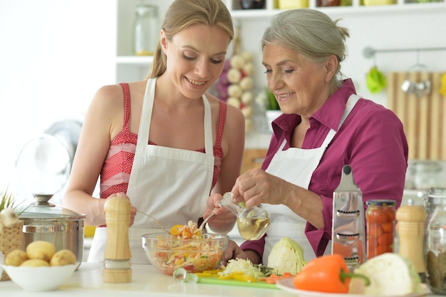 Glimlachende oudere moeder en volwassen dochter koken samen in de keuken