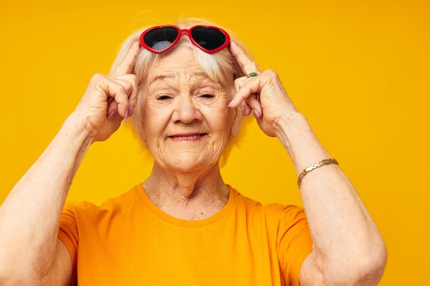 Glimlachende oudere vrouw in casual tshirt zonnebril gele achtergrond