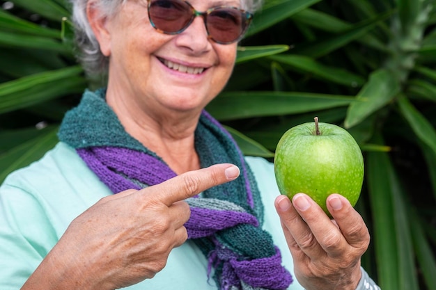 Foto glimlachende oudere vrouw met een appel in haar hand terwijl ze tegen de plant staat