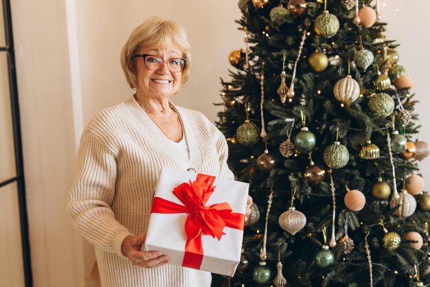 Glimlachende oudere vrouw met een geschenk bij de kerstboom