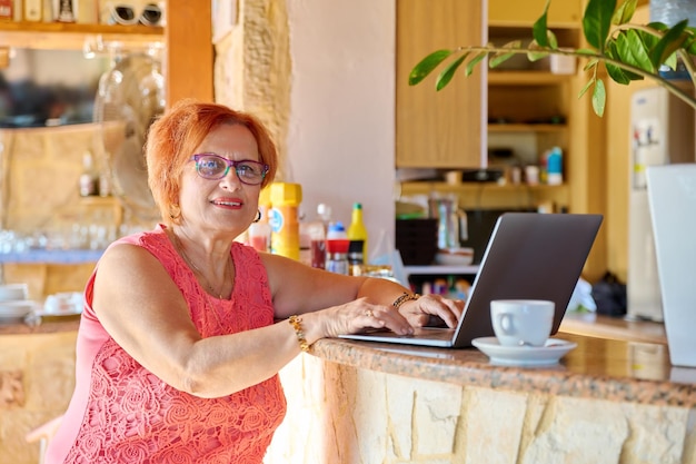 Glimlachende positieve bejaarde die het laptop scherm bekijkt