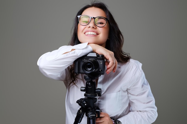 Glimlachende, positieve brunette vrouw in brillen die foto's maken met een professionele fotocamera. Geïsoleerd op grijze achtergrond.