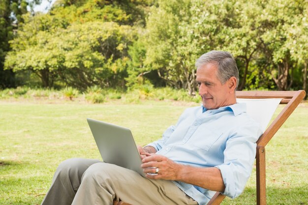 Glimlachende rijpe mens die zijn laptop met behulp van