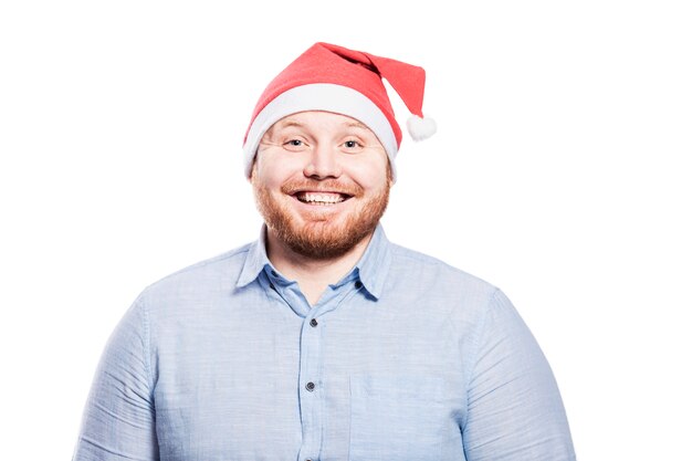 Glimlachende roodharige man met een baard in een blauw shirt en in een kerstman hoed. Detailopname.