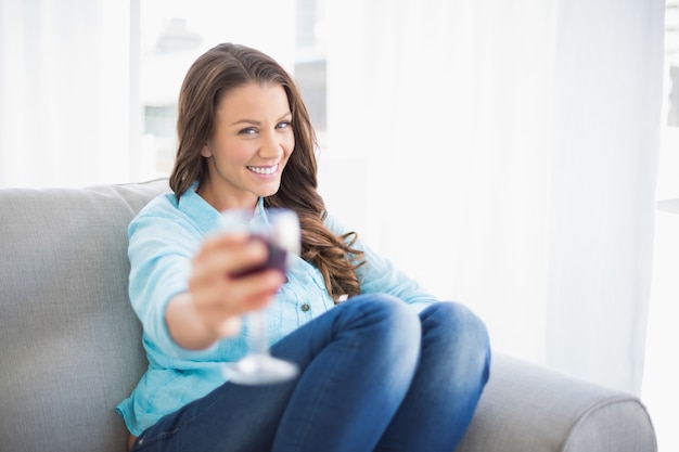 Glimlachende schitterende vrouw die glas rode wijn aanbiedt