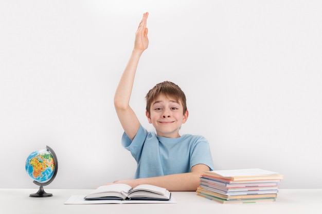 Glimlachende schooljongen stak zijn hand op tijdens de les uitstekende student weet het antwoord portret van student aan tafel naast notitieboekjes