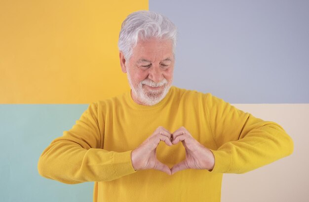 Glimlachende senior blanke man met baard die hartvorm maakt met handen Knappe senior grootvader die op een kleurrijke geïsoleerde achtergrond staat en liefde en gevoel uitdrukt