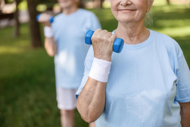 Glimlachende senior vrouw doet oefeningen met dumbbell training met vriend in groen park