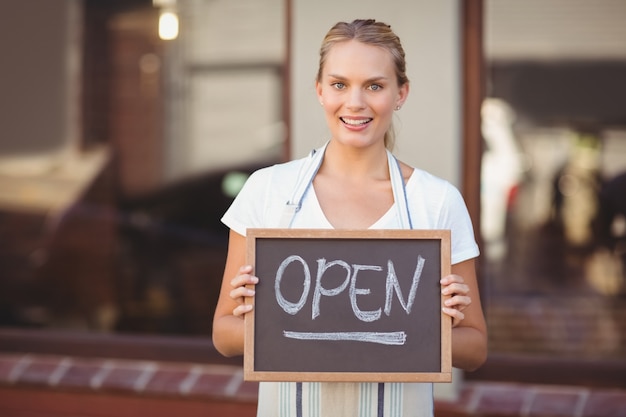 Glimlachende serveerster die bord met open teken toont