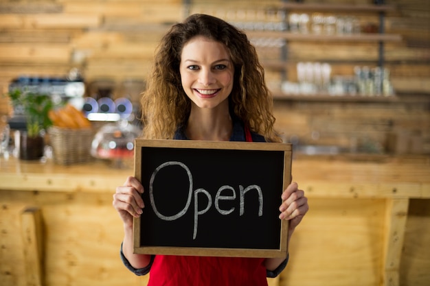 Glimlachende serveerster die lei met open teken in koffie toont