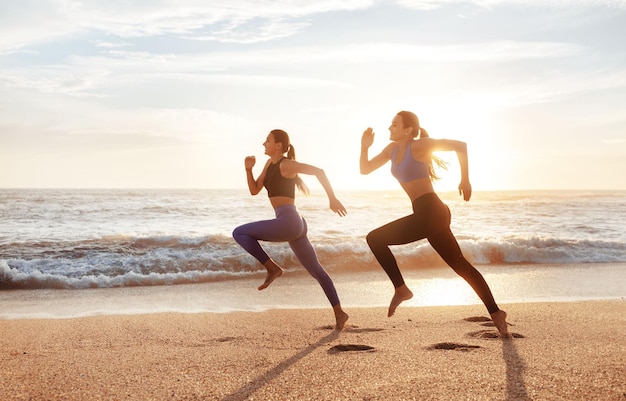 Glimlachende snelle slanke jonge blanke vrouwen genieten van ochtendtraining terwijl ze bevriezen in de lucht op zeestrand