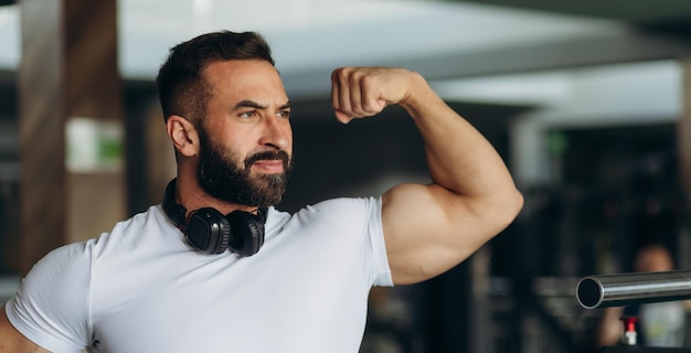 Glimlachende sportman in witte t-shirt die zijn spieren in de sportschool laat zien